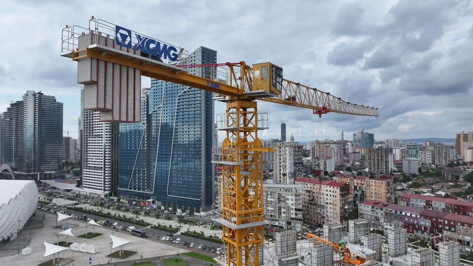 Real tower crane operating on an urban construction project with high-rise development in the background
